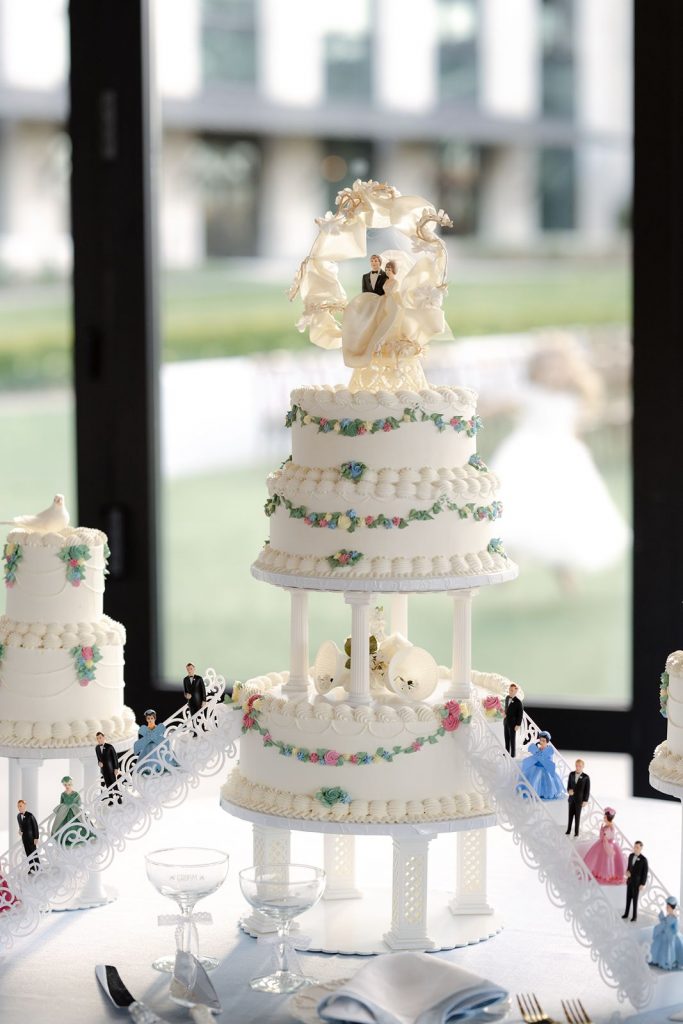 A multi-tiered vintage wedding cake complete with detailed piping and custom toppers featuring the bride, groom, their bridesmaids, and groomsmen