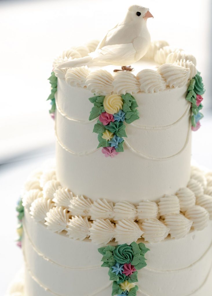 A multi-tiered vintage wedding cake with detailed piping and a white bird topper