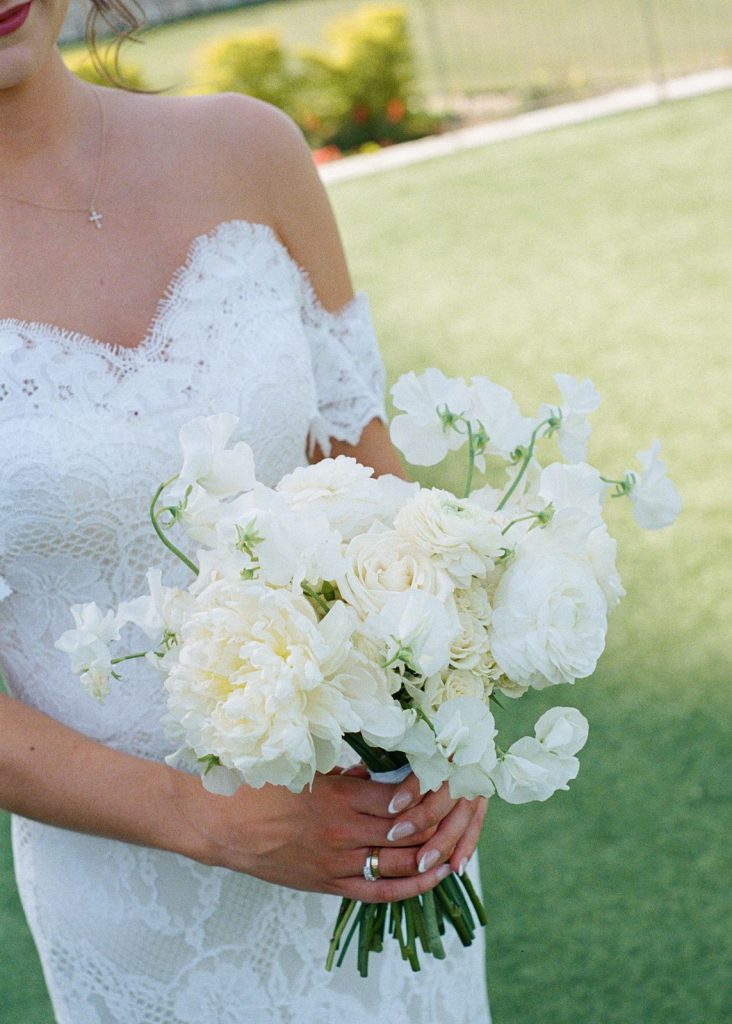 Bride at Omni Barton Creek holding white bridal bouquet. The bouquet features sweet pea, roses, and peony, giving it a fresh, lush, and classic style that compliments her vintage lace dress